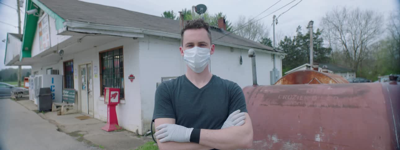 A man standing outside of a small store wearing a face mask and gloves
