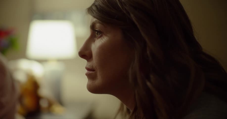A woman sits and listens in a room lit by a lamp