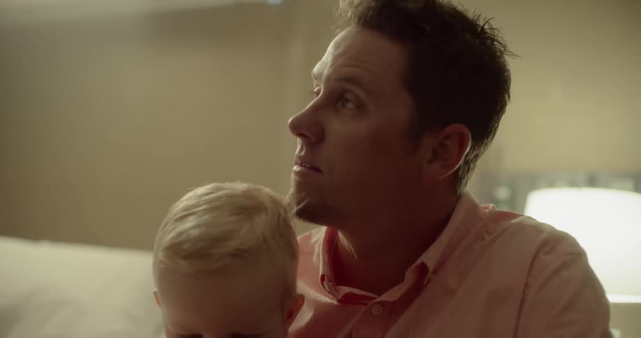 Man sits near bed with child playing with a toy