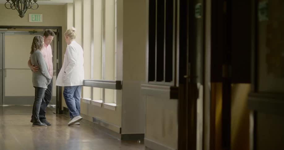 A doctor gives bad news to a couple in a hospital hallway