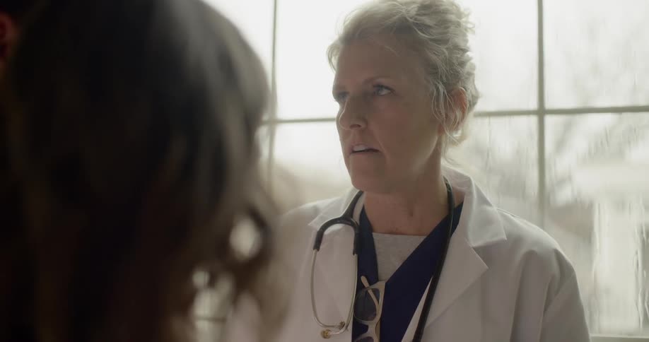 A doctor chats with her patient in front of a large window