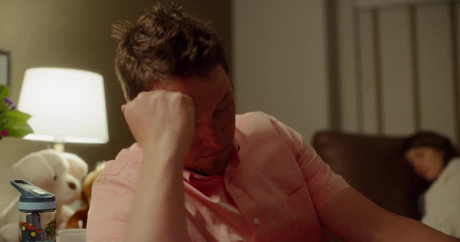 Man leans on arm thinking while woman sleeps behind him