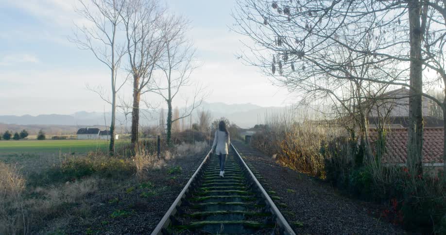 A woman walks down an empty railroad track