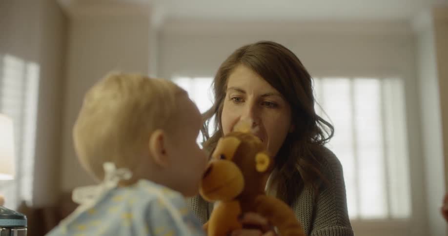 A woman using a stuffed animal to play with a baby as a man brings up a cup of water