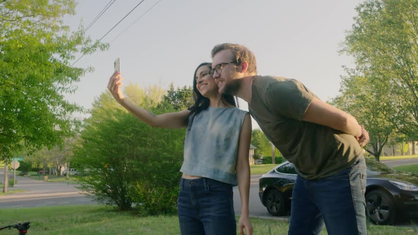 A woman and man have a video call using a cell phone while standing in their front yard
