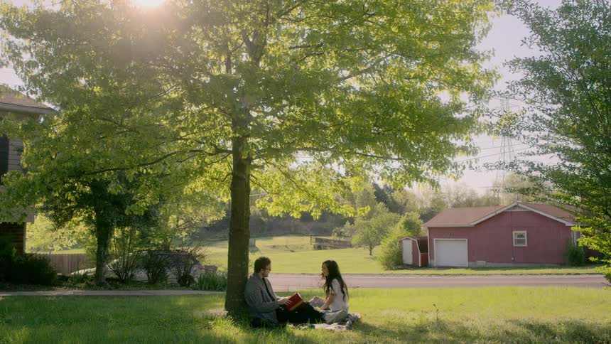 Couple sit on blanket outdoors under a tree talking