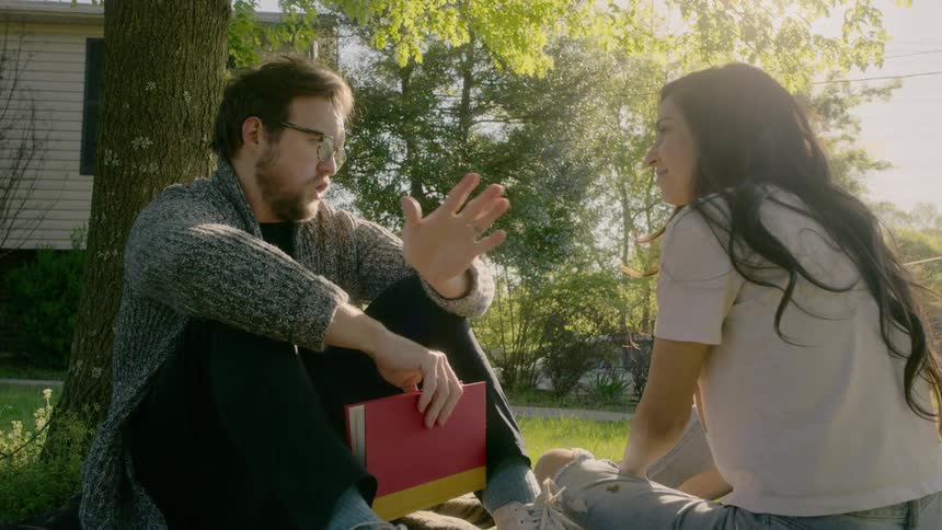 A man and woman chat while sitting on a blanket in their yard