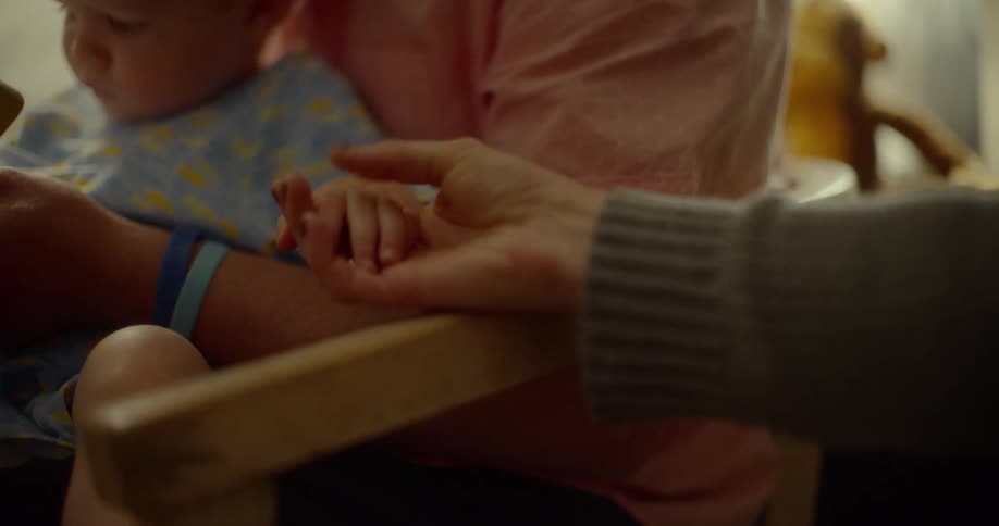 A man holds his son while a woman reaches over and holds his hand