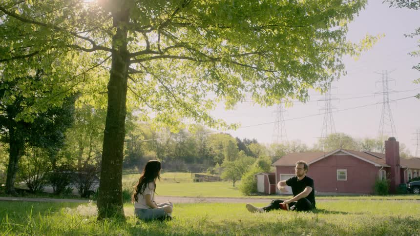 A man and a woman sitting on the grass underneath a tree talking