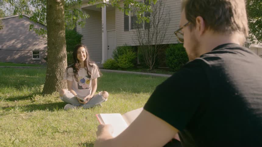 Couple sitting on the grass under a tree reading a book at day