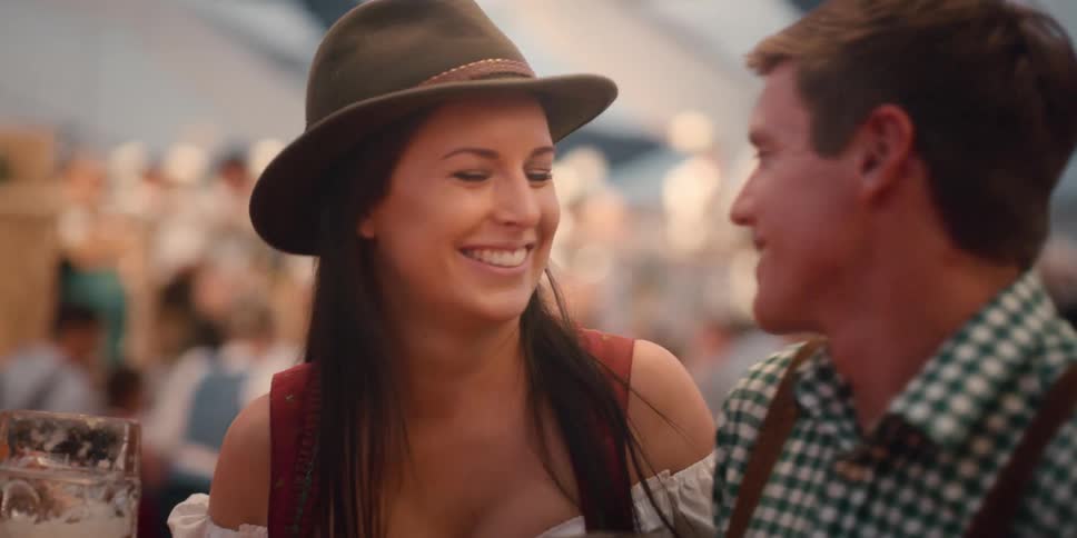 A couple holding beer steins smile and kiss each other at an oktoberfest party