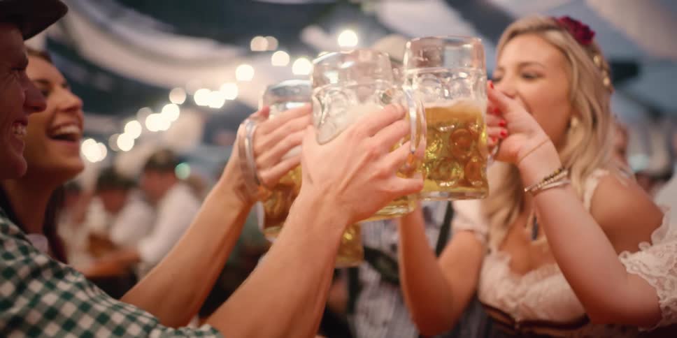 Friends sit around table clinking beer mugs for oktoberfest