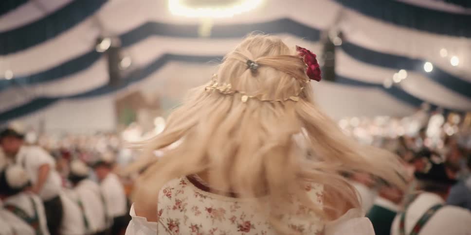 A blonde woman turns her head and laughs over her shoulder as she walks through an oktoberfest party in a tent