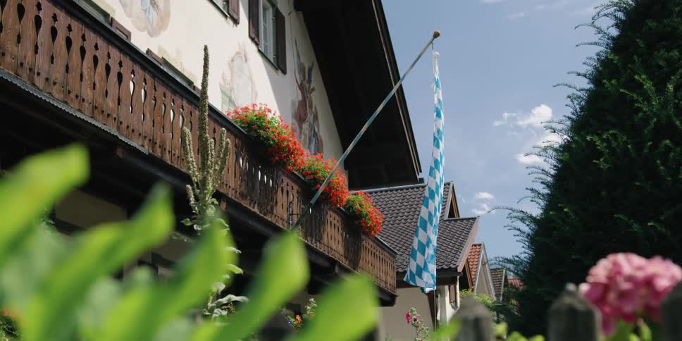 A blue and white checkered banner sways in the breeze hanging from a balcony overlooking flowers in a garden
