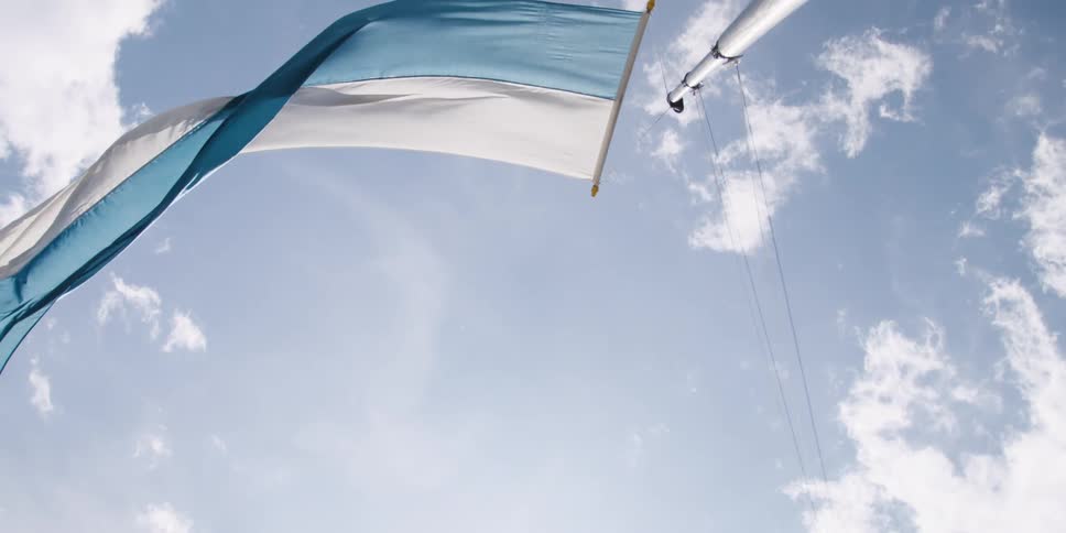 Big flag on flagpole waves in the wind in a sunny day