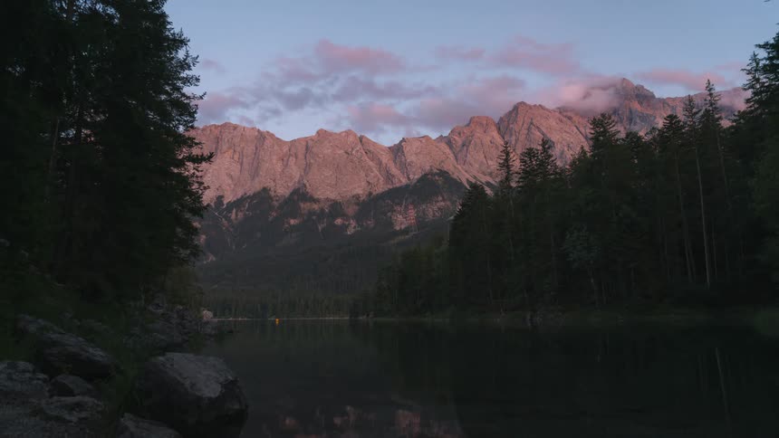 Sun tints clouds reddish pink as they pass over mountains forest and lake