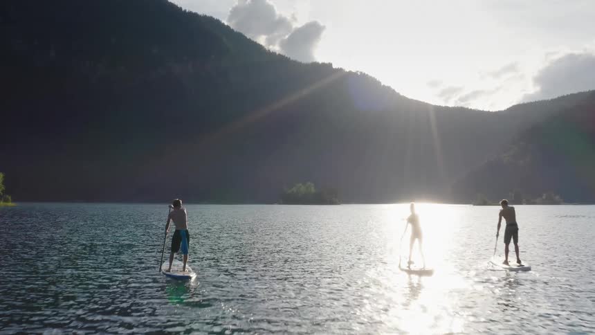 Trio of men ride paddle boards toward the mountains the sun is peaking over
