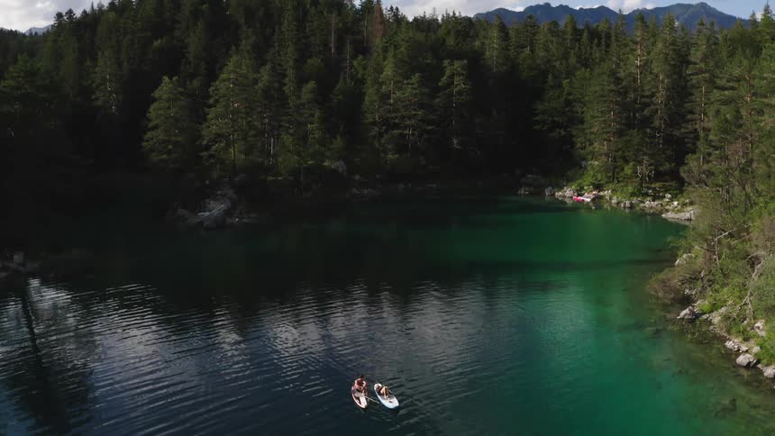 Man and woman drift on paddleboards in middle of forest
