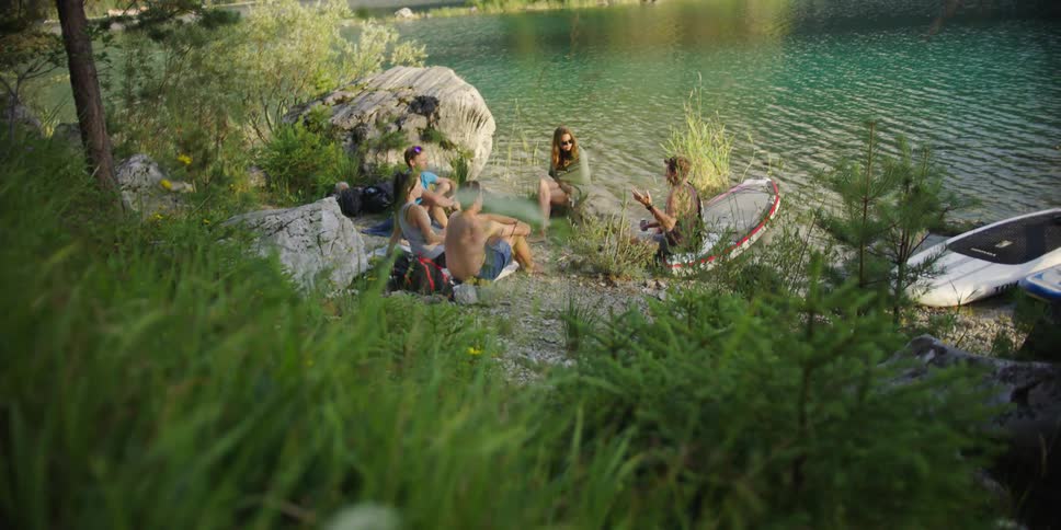 A group of people sitting together chatting on the shore of a lake