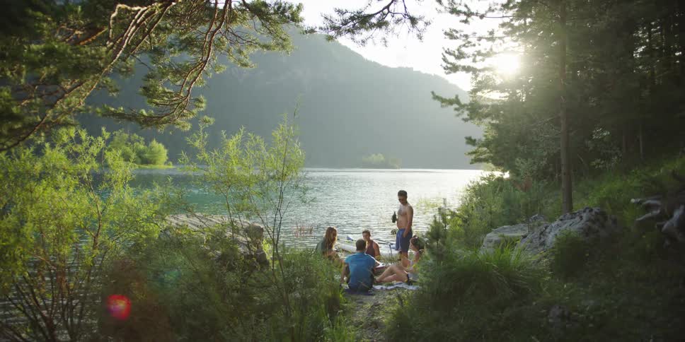 A group of friends drink while sitting on the side of a lake