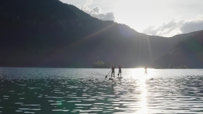 Two men and a woman paddle boarding on a lake
