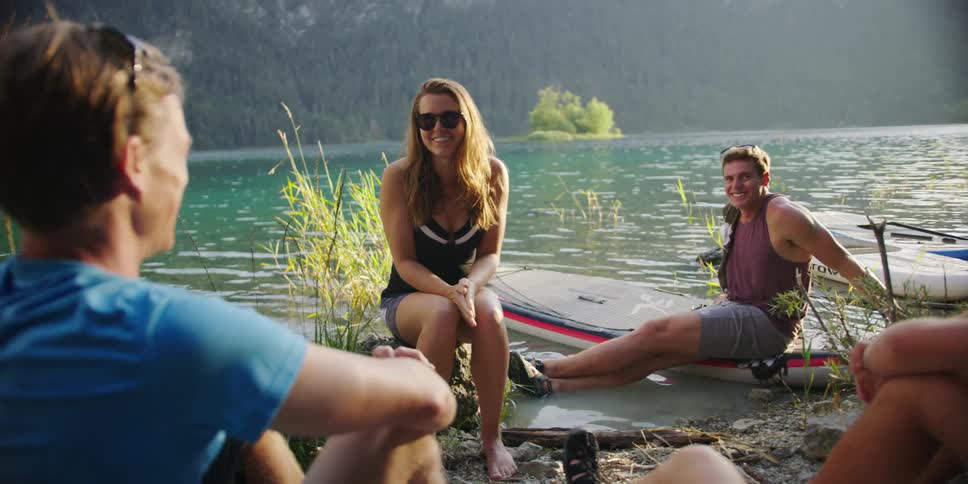 A group of friends sit outside a lake and talk