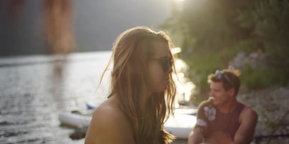 A young woman sitting on the shore of a lake talking with other people