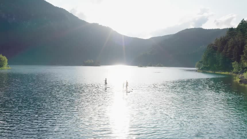 Three people paddle board in a lake at the base of a canyon