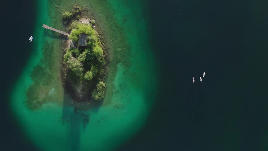 An island with a pier and trees with people paddle boarding next to it