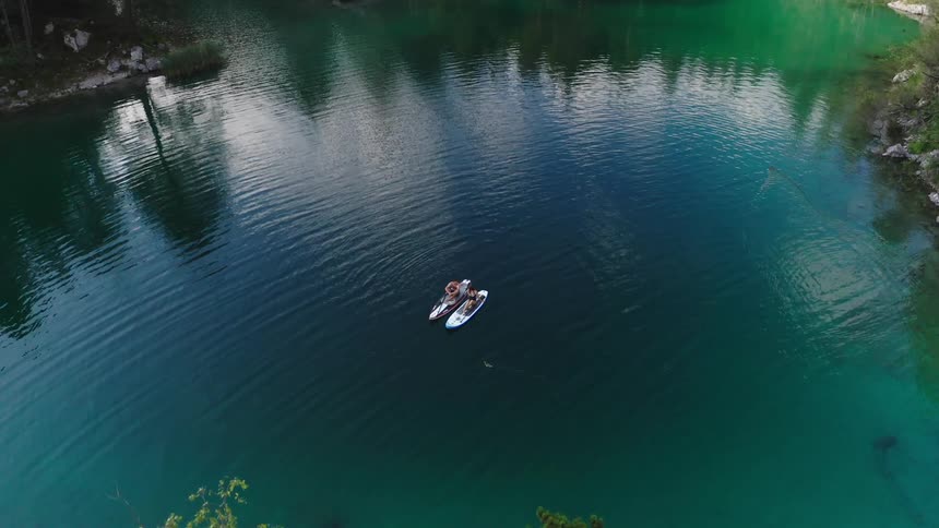 Man and woman sitting on the paddle boards watch the high mountain landscape on the lake