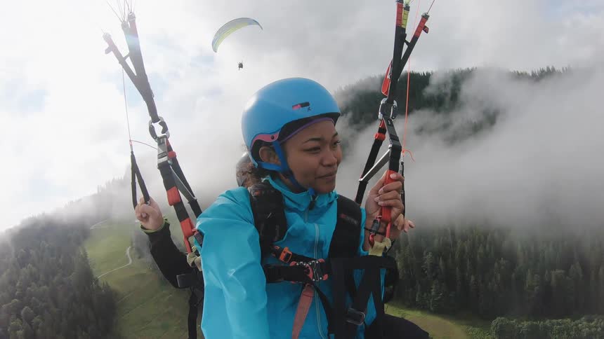 A woman and a man paragliding with hills and forests in the background