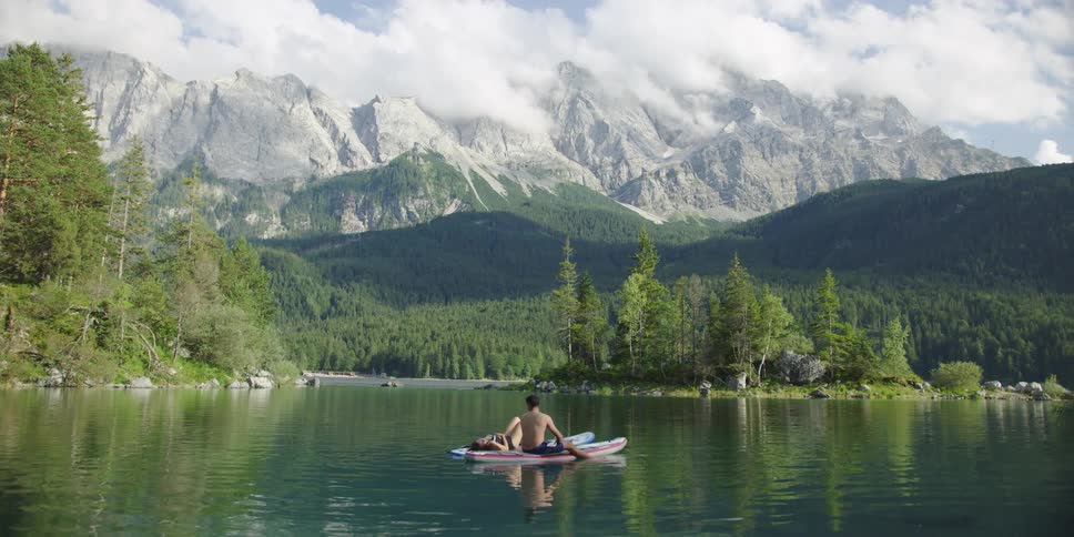 Two people sit on their surfboards resting in the lake