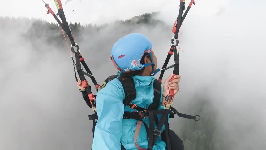Man and woman parasail over fog obscured mountain forest