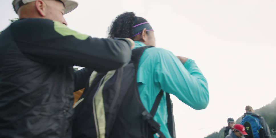 Man helps woman wear backpack in the mountains