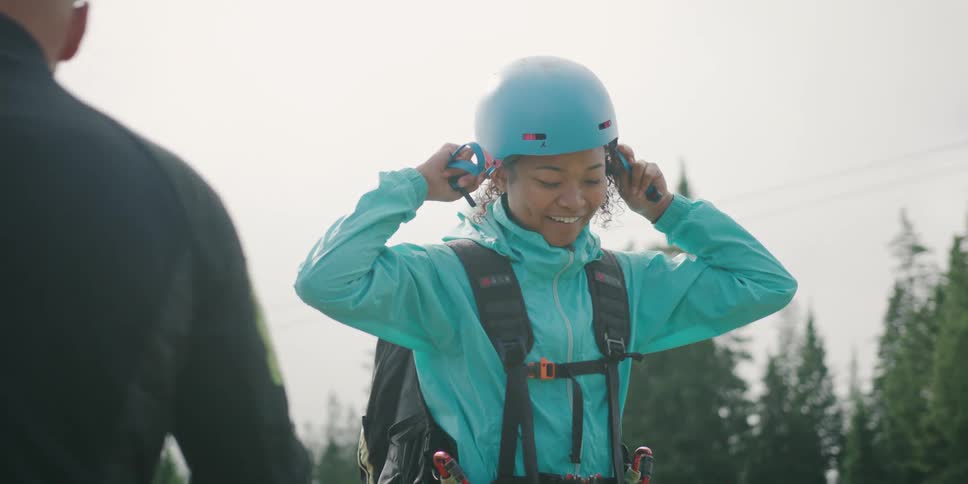 A young woman putting on a helmet while listening to an older man talk to her