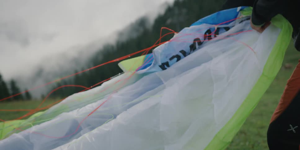 A man untangles the lines of a sail preparing to paraglide on a fog covered slope