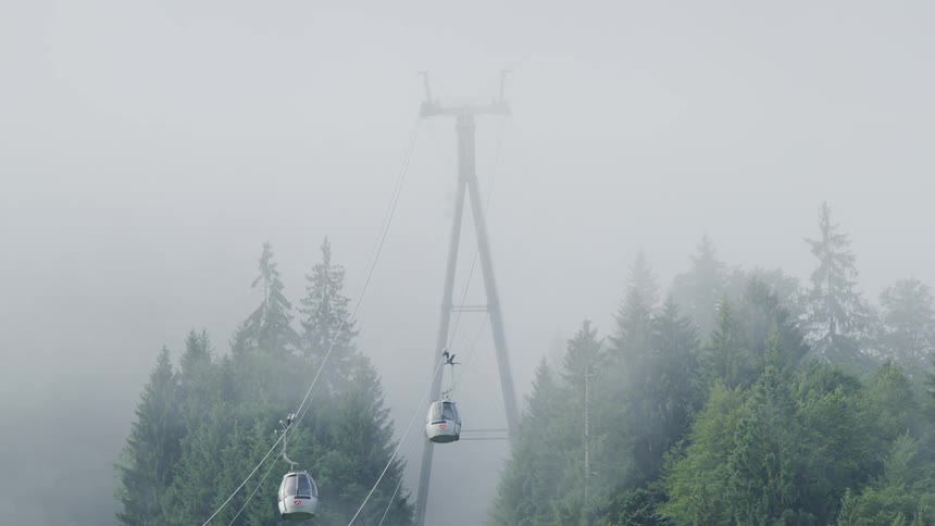 Gondolas on a lift go up and down through fog and over trees