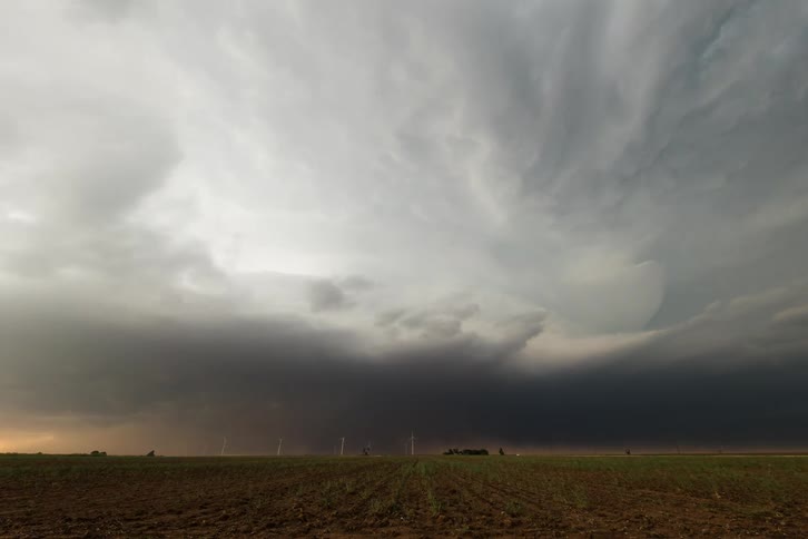 A storm with dark clouds begins to form a funnel cloud over a rural area