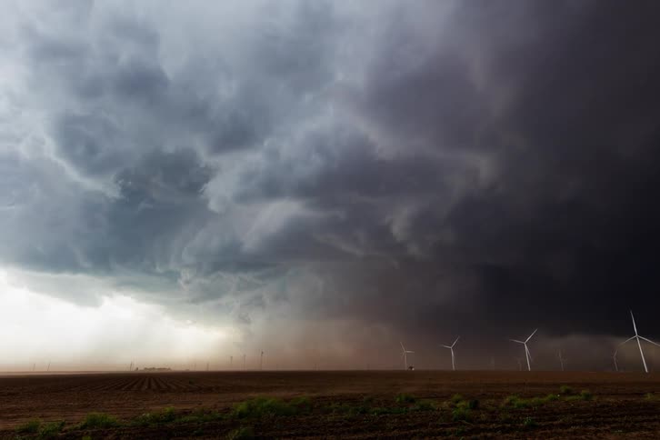 Storm clouds swirl and high winds dust over the field and wind turbines