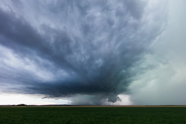A grassy plain with clouds and a tornado in the background