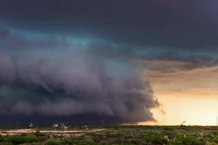 A grassy plain with vehicles driving by with lightning and rain clouds above