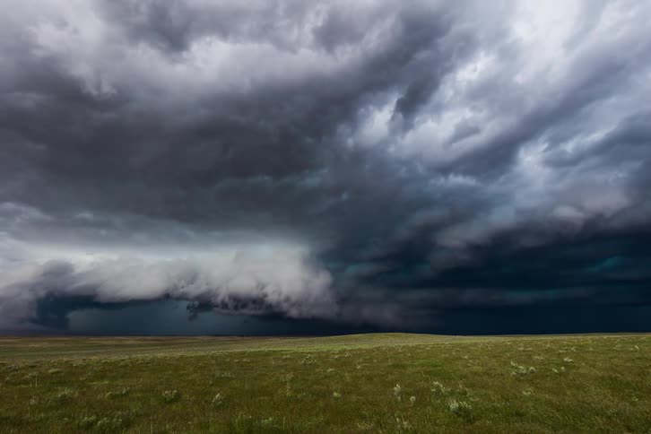 Storm clouds gather and expand over a green grass field