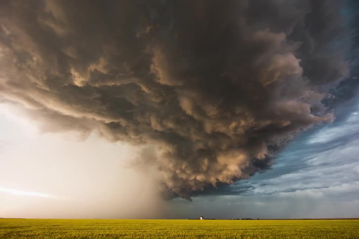 A grassy field with storm clouds moving above