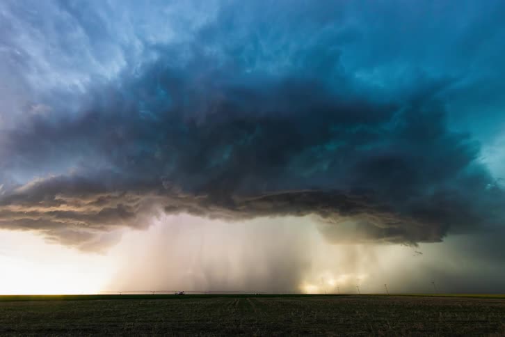 Rain and thunderstorm clouds surge over a field and road with lightning flashes