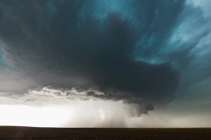 Storm clouds releasing rain and lightning over plains at day