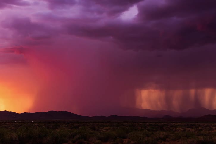 A strong downburst of rain over desert mountains at sunset