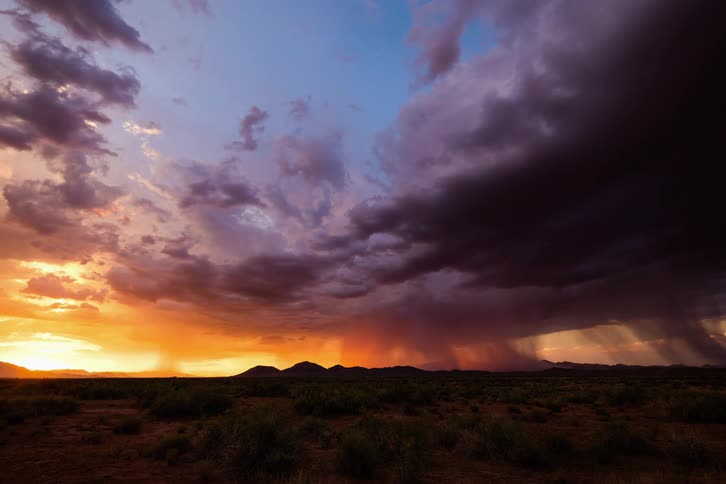 A desert with rain clouds above and mountains in the background