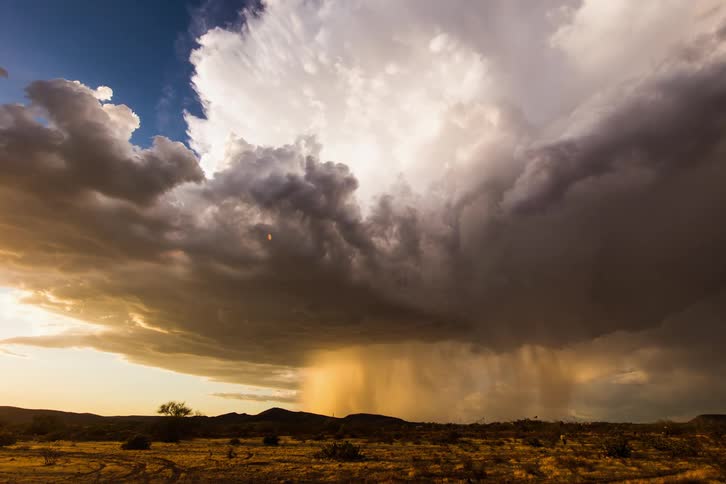 Storm clouds release rain over desert at sunset