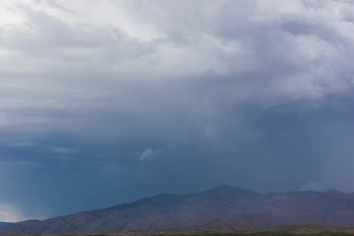 Storm clouds swirl and gather over a ridge and lightning flashes during a thunderstorm