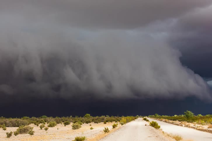 Storm clouds gather and swirl over desert brush and road